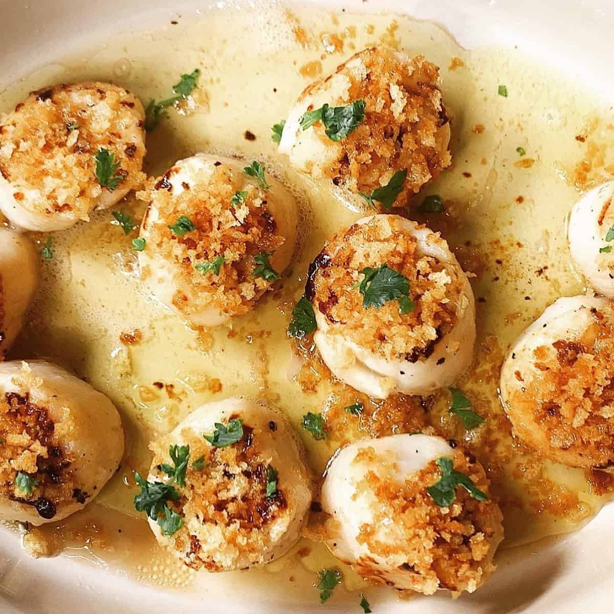 Panko crusted scallops in baking dish with butter and topped with parsley