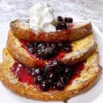 Sourdough French toast on a white plate with whipped cream and blueberry syrup.
