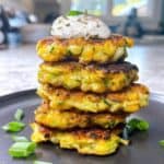 Zucchini corn fritters stacked with green onion and sour cream garnish