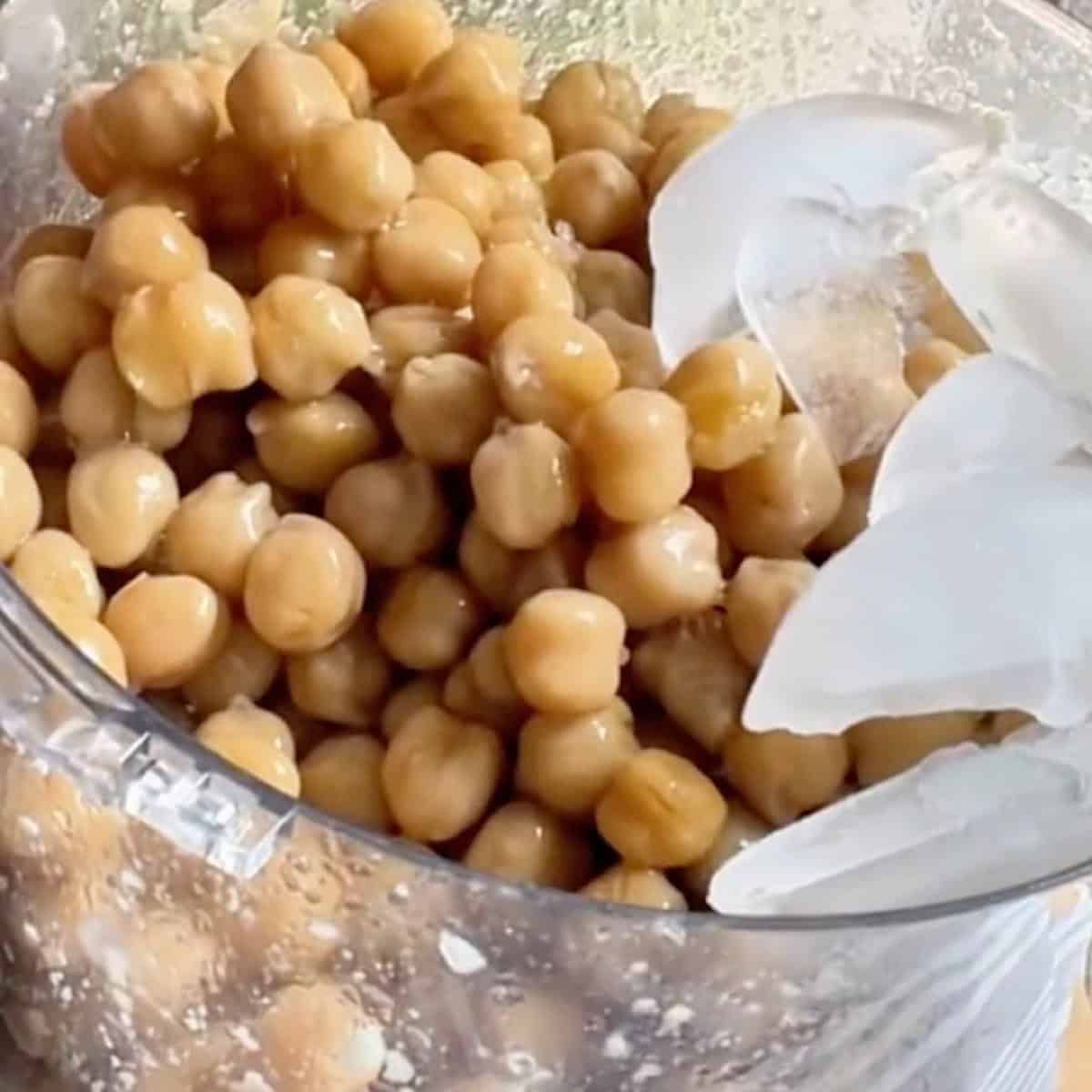 Placing ice on top of the chickpeas and other ingredients in food processor.