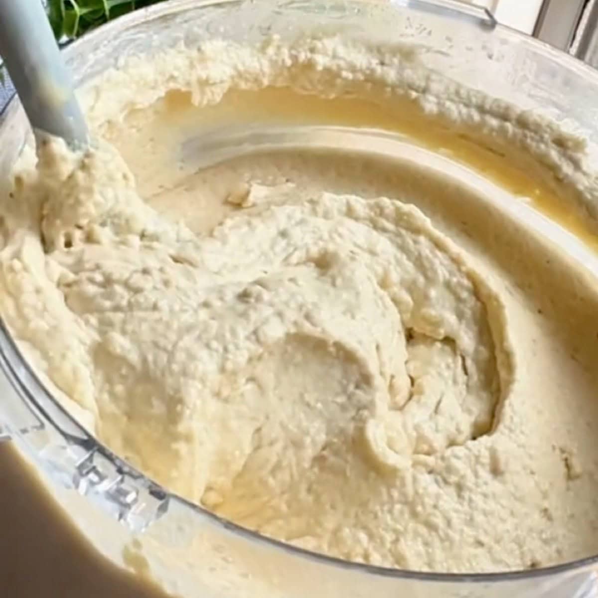Rubber spatula showing the consistency of hummus in the food processor.