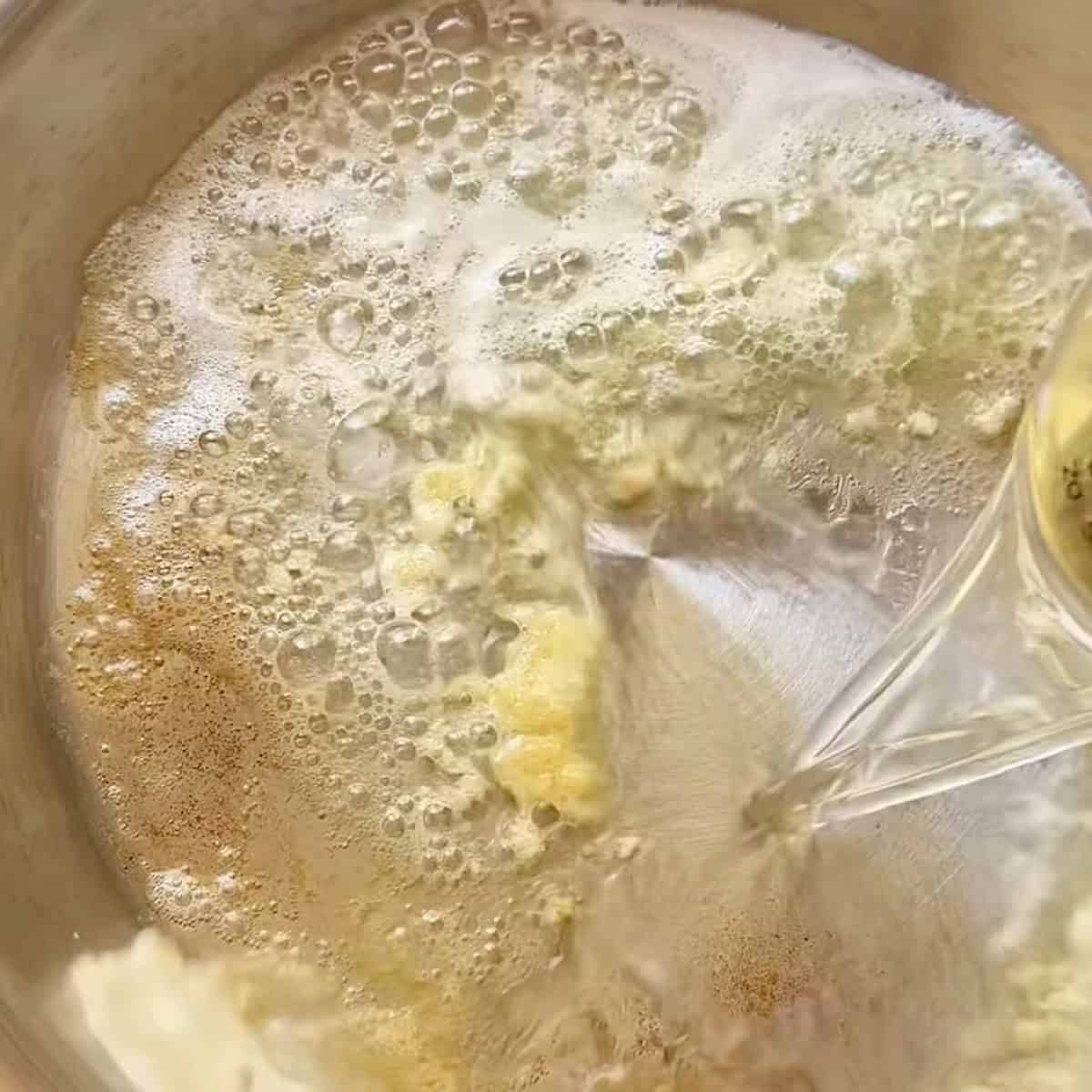 Pouring white wine into the skillet of garlic butter.