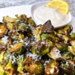 Crispy air fryer Brussels sprouts with parmesan and garlic aioli feature image close up with dipping sauce and lemon.