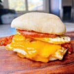 Bacon egg and cheese English muffin breakfast sandwich feature image. close up of double decker sandwich with cheese melted.