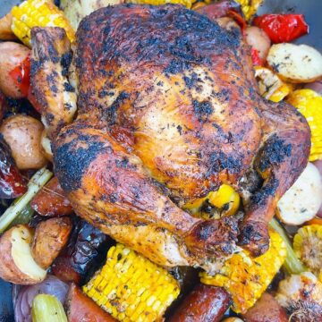 Cajun roasted chicken with andouille sausage and potatoes hero shot. close up of crispy skin roast on vegetables and sausage fully cooked with garnish.