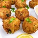 Crispy crab bites with remoulade on a platter with lemon and sauce.