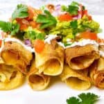Air fryer flautas with refried beans and guacamole stacked with all of the toppings.