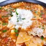 Lasagna soup in black bowl with melty cheese topping and basil.