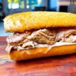 A mojo pork sandwich with cheese melted on a hoagie roll and stuffed with mojo pork.