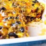 Cheesy layered taco casserole with ground beef in baking dish with inside showing after served.