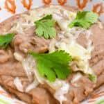 easy and authentic mexican refried beans instant pot feature image close up with Monterey Jack cheese and cilantro in a decorative bowl
