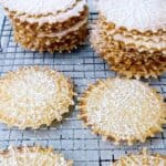 traditional Italian pizzelles with anise feature image close up of cookies on wire rack with powdered sugar.