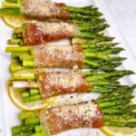 oven baked prosciutto wrapped asparagus bundles with parmesan feature image close up on platter with lemon wedges and topping