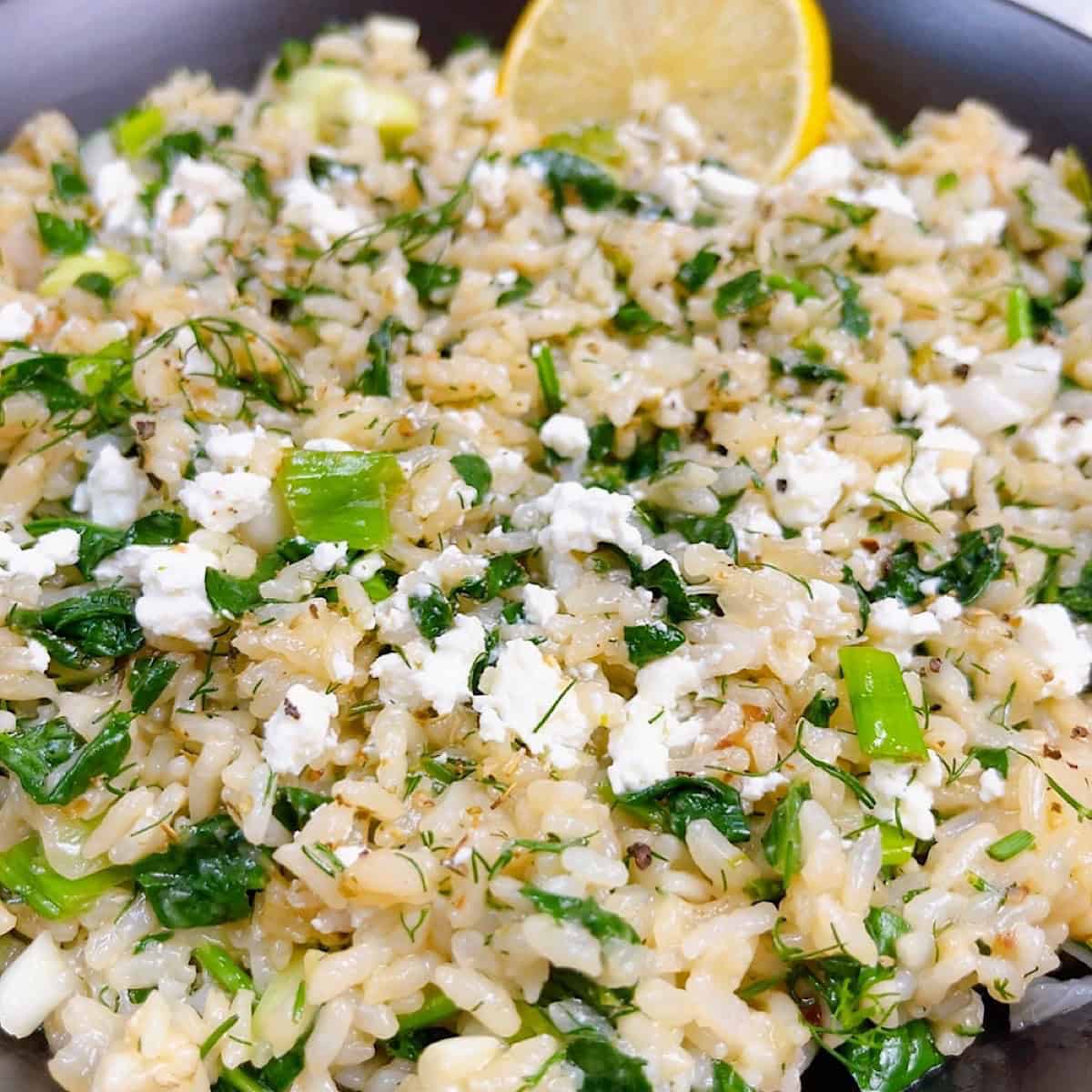 spanakorizo greek spinach rice with lemon and dill in the instant pot feature image close up in black bowl with lemon and feta crumbled.