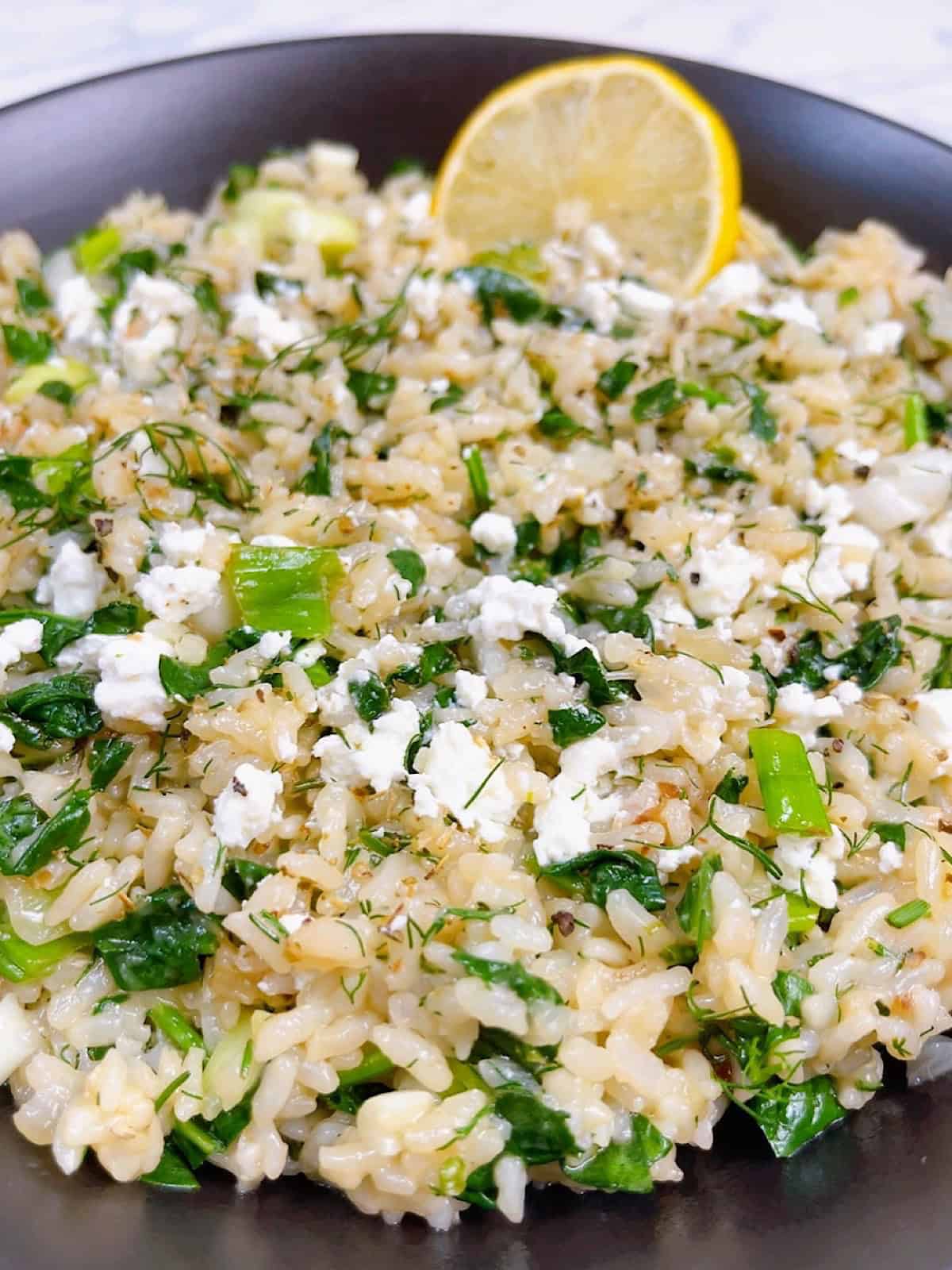 spanakorizo greek spinach rice with lemon and dill in the instant pot hero image close up in black bowl with lemon and feta crumbled.