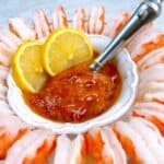 Shrimp cocktail platter with dipping spoon and lemon garnish.