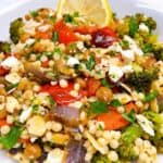 Couscous with roasted veggies, chickpeas, and feta feature image close up in bowl with lemon garnish.