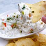 Easy dill pickle dip with Grillo's feature image holding a chip with dip and bowl in background.