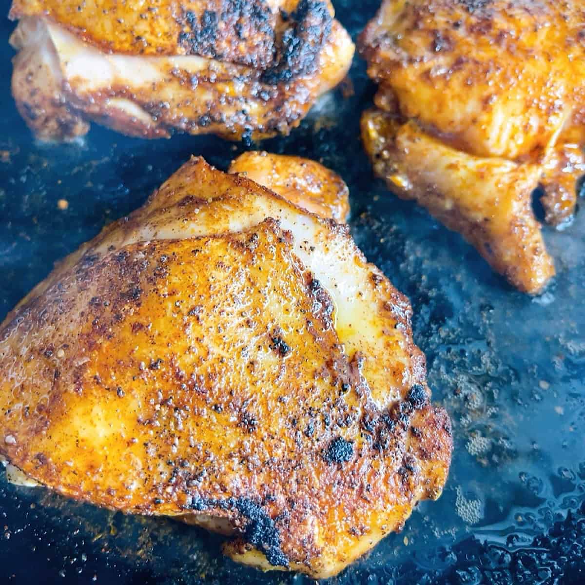 Chicken thighs being seared in cast iron skillet.