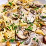 Creamy garlic mushroom pasta recipe feature image. Close up of dish in white bowl with garnish.