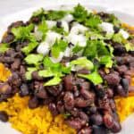 Instant Pot Cuban black beans over yellow rice with cilantro and onion as garnish.