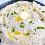 Mashed potatoes in a black bowl with a melted butter pat and parsley.