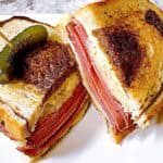 A cold pastrami sandwich sliced in half and stacked with a toothpick and pickle on top.