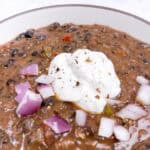 A bowl of creamy black bean soup topped with sour cream and onion.