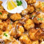 Crispy cauliflower bites in a white bowl with garnish and a bowl of garlic aioli for dipping.