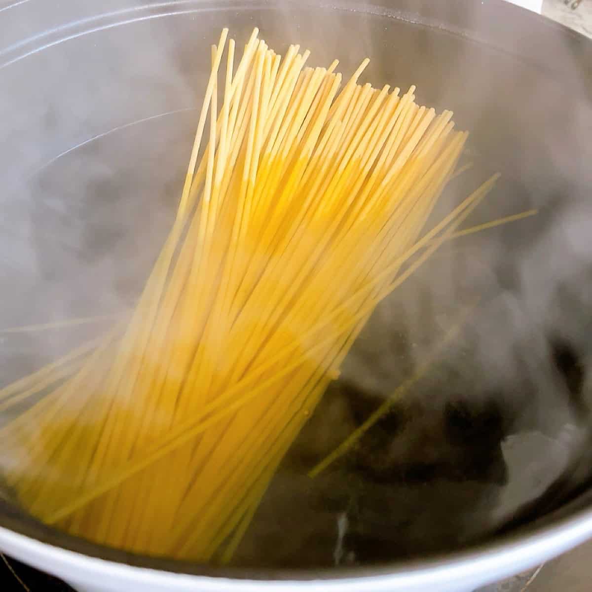 Placing bucatini pasta into a pot of salted boiling water.