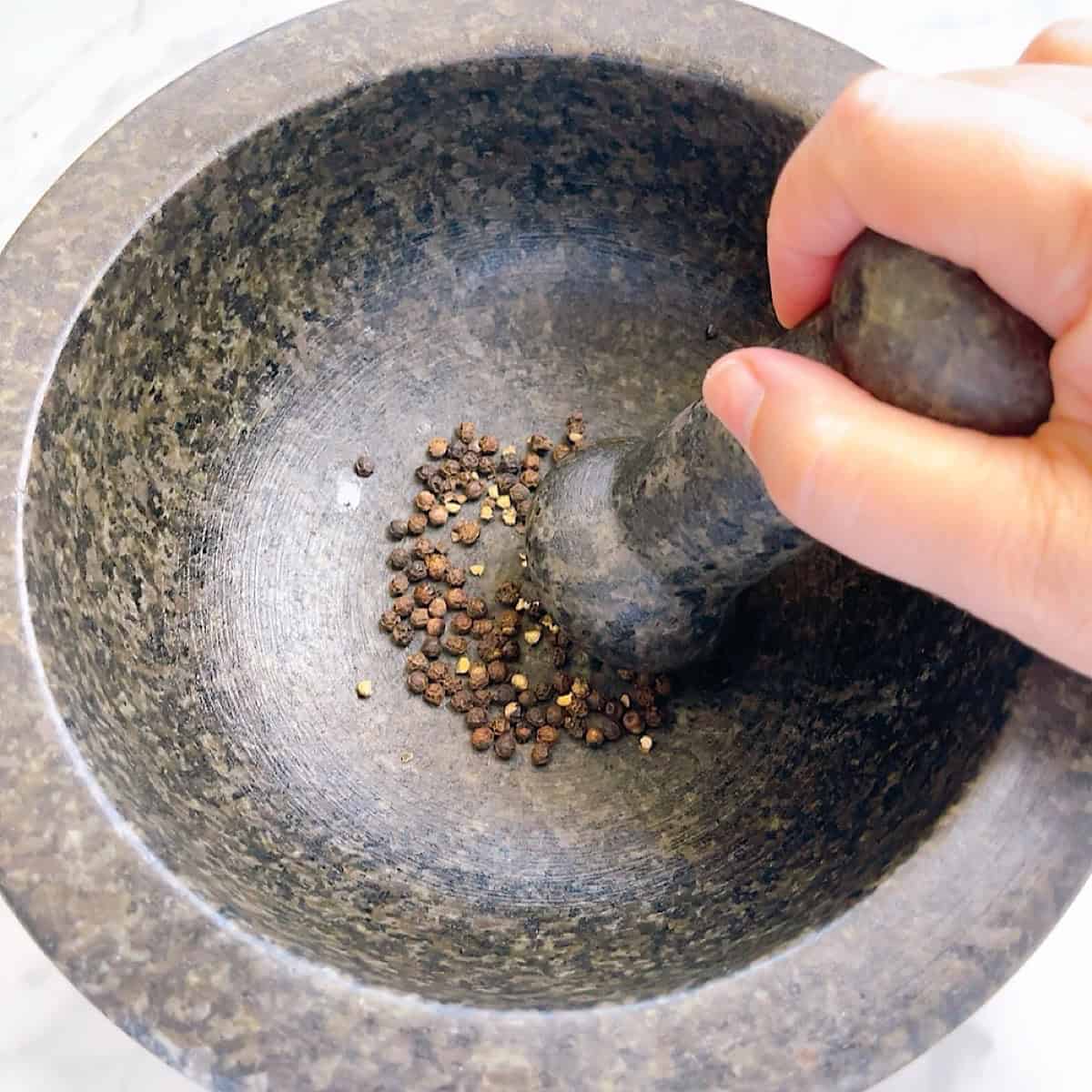 Crushing toasted whole peppercorns in a mortar and pestle.