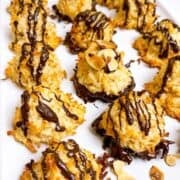 Coconut macaroons on serving platter drizzled in chocolate with toasted slivered almonds on top.