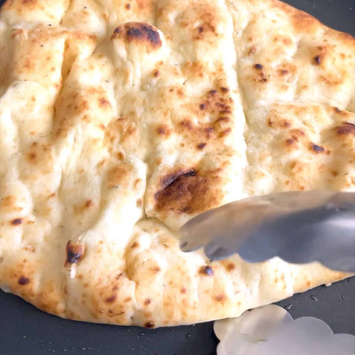 Naan bread lightly brushed with olive oil warming in a skillet.