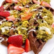 Chocolate waffles quartered on a platter with pistachio filling, chocolate drizzle, and crunchy nut topping.