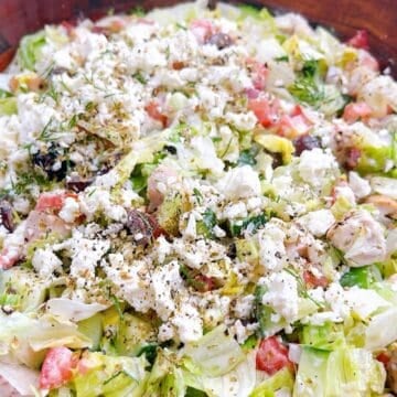 A tossed chopped Greek salad in wooden salad bowl with Greek yogurt dressing.