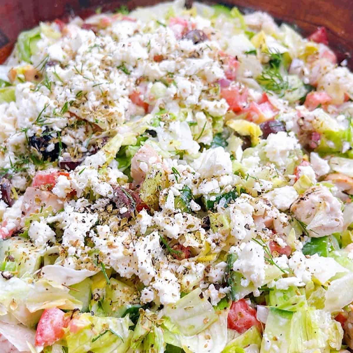 A tossed chopped Greek salad in wooden salad bowl with Greek yogurt dressing.