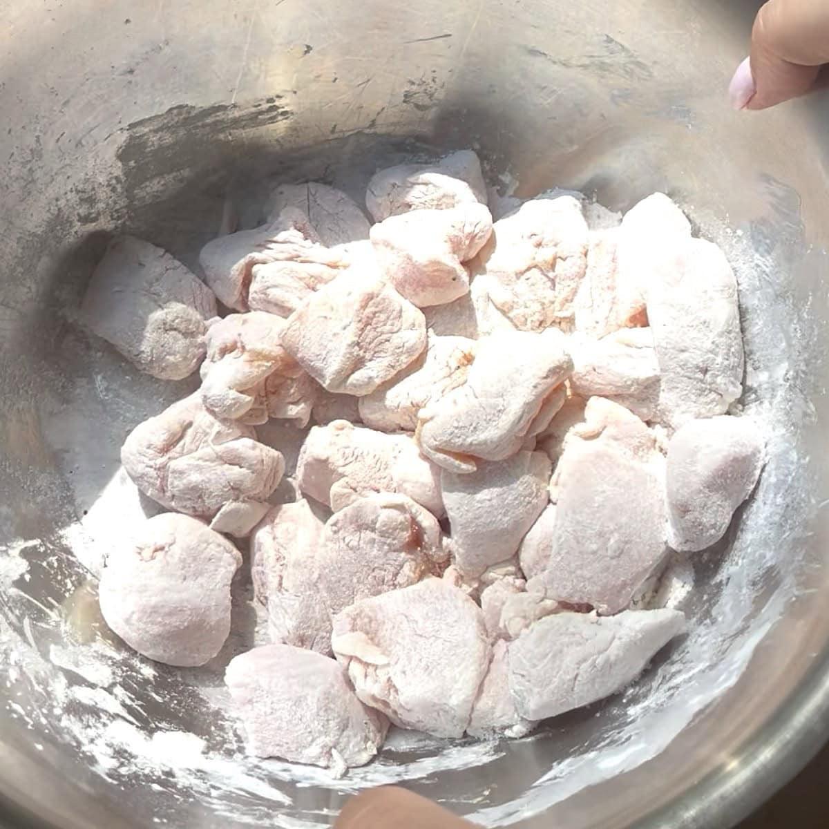 Cubed chicken being coated in cornstarch, flour, and seasoning.