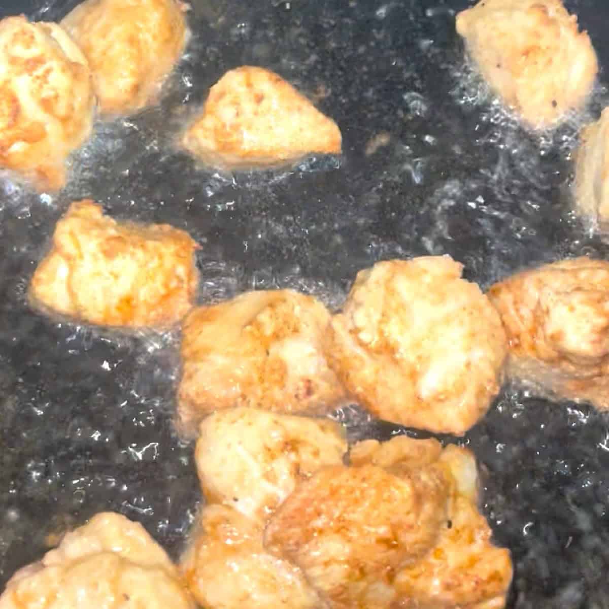Chicken pieces frying in skillet.