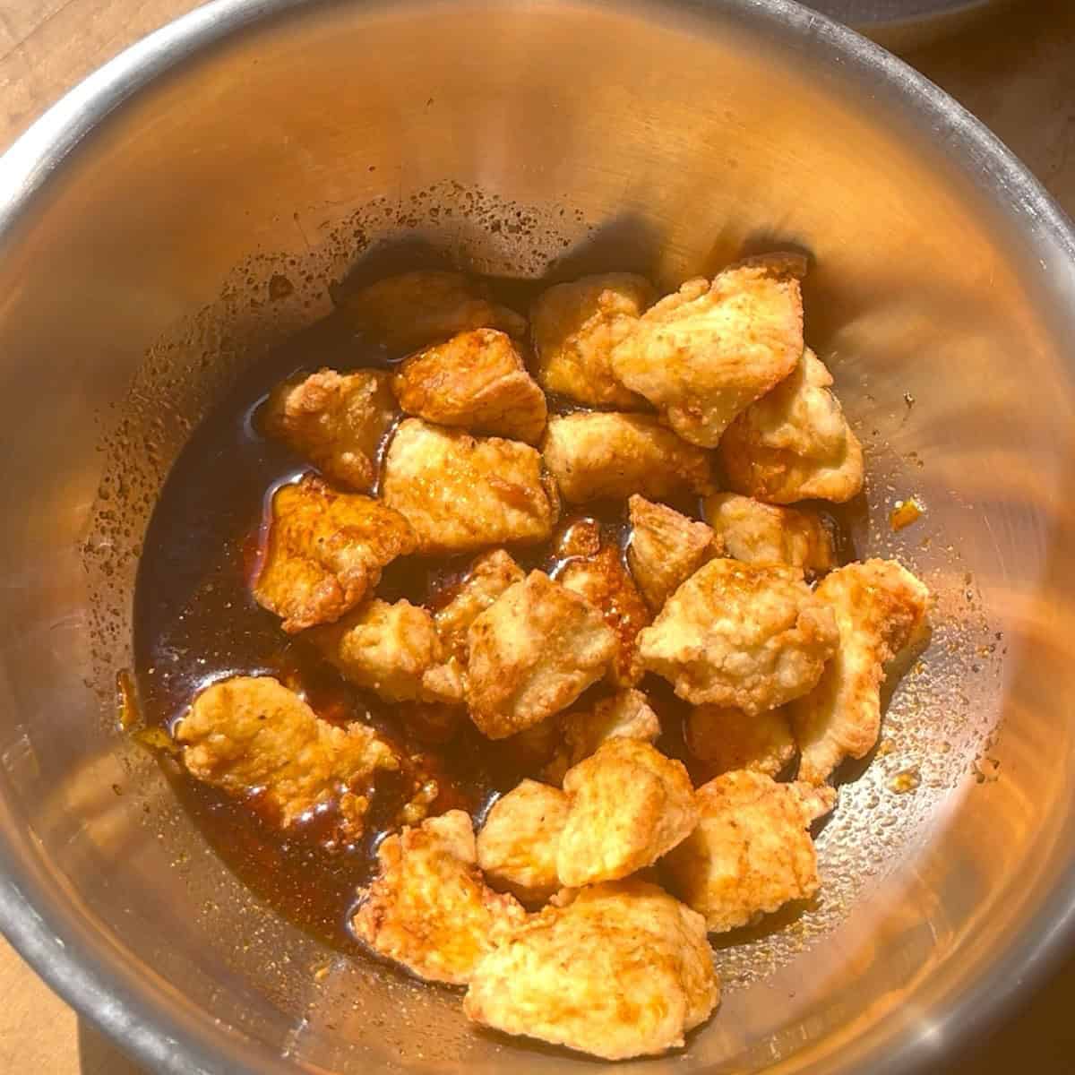 Fully cooked chicken pieces being tossed in the orange sauce.