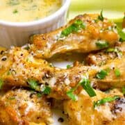 Garlic parmesan wings with garnish on a plate beside garlic parmesan dipping sauce.
