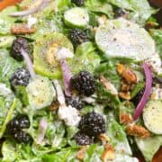 Kiwi salad with blackberries and pecans tossed with dressing in a wooden bowl.