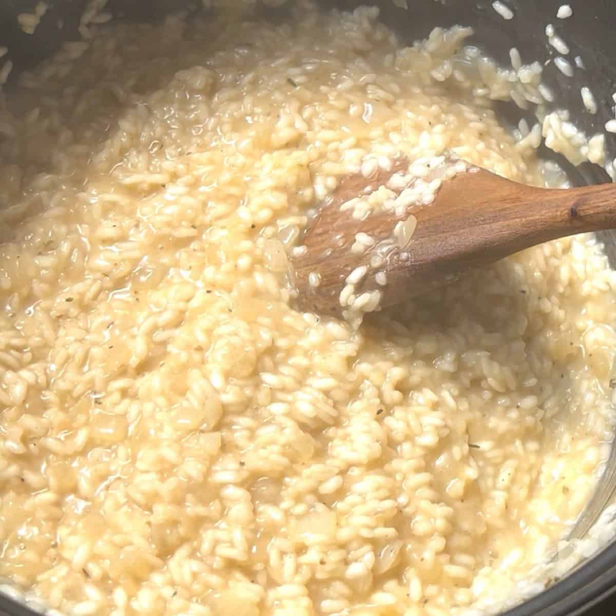 Creamy risotto cooked down with wooden spoon in dutch oven.
