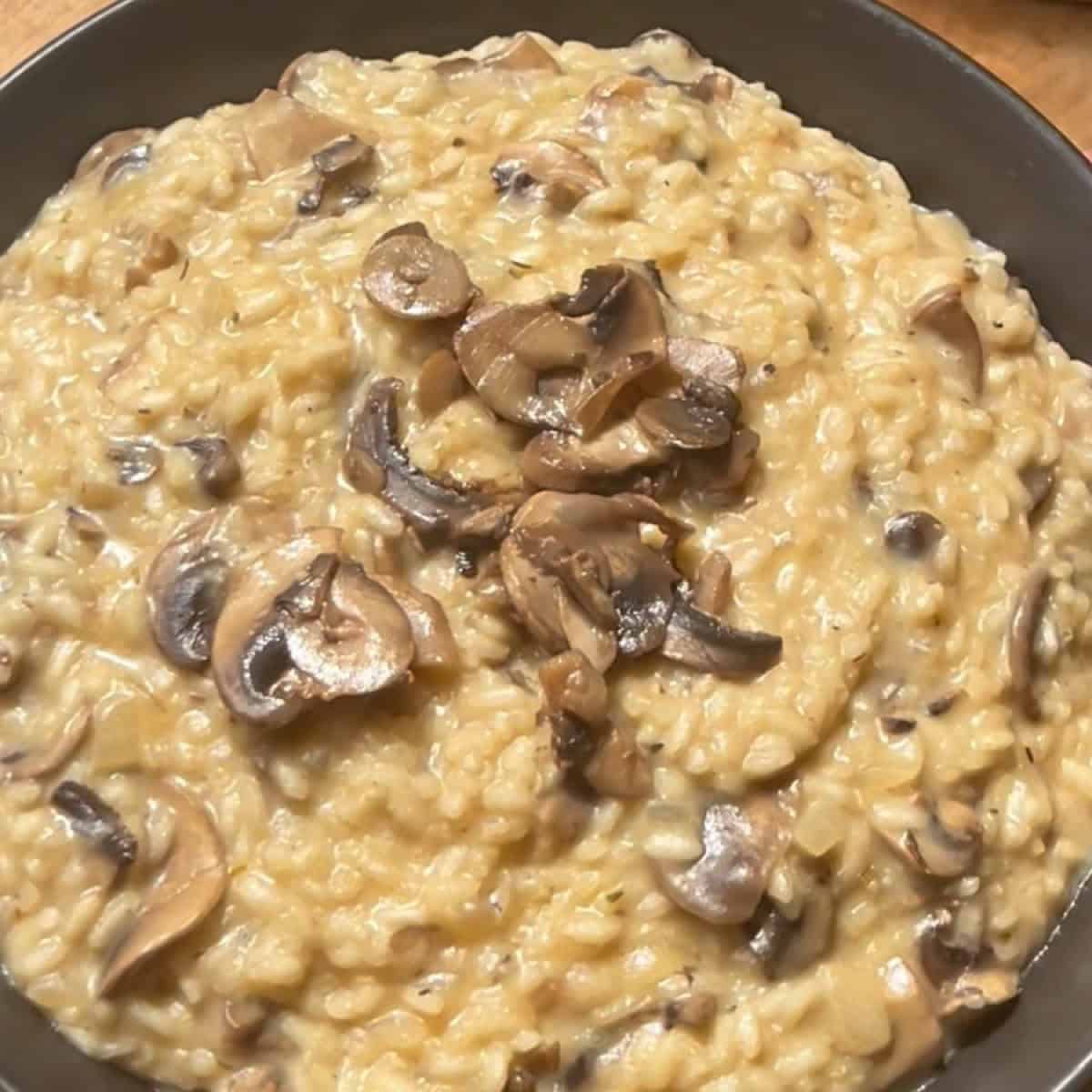 Mushroom truffle risotto in a black serving bowl with mushrooms and parmesan on top.