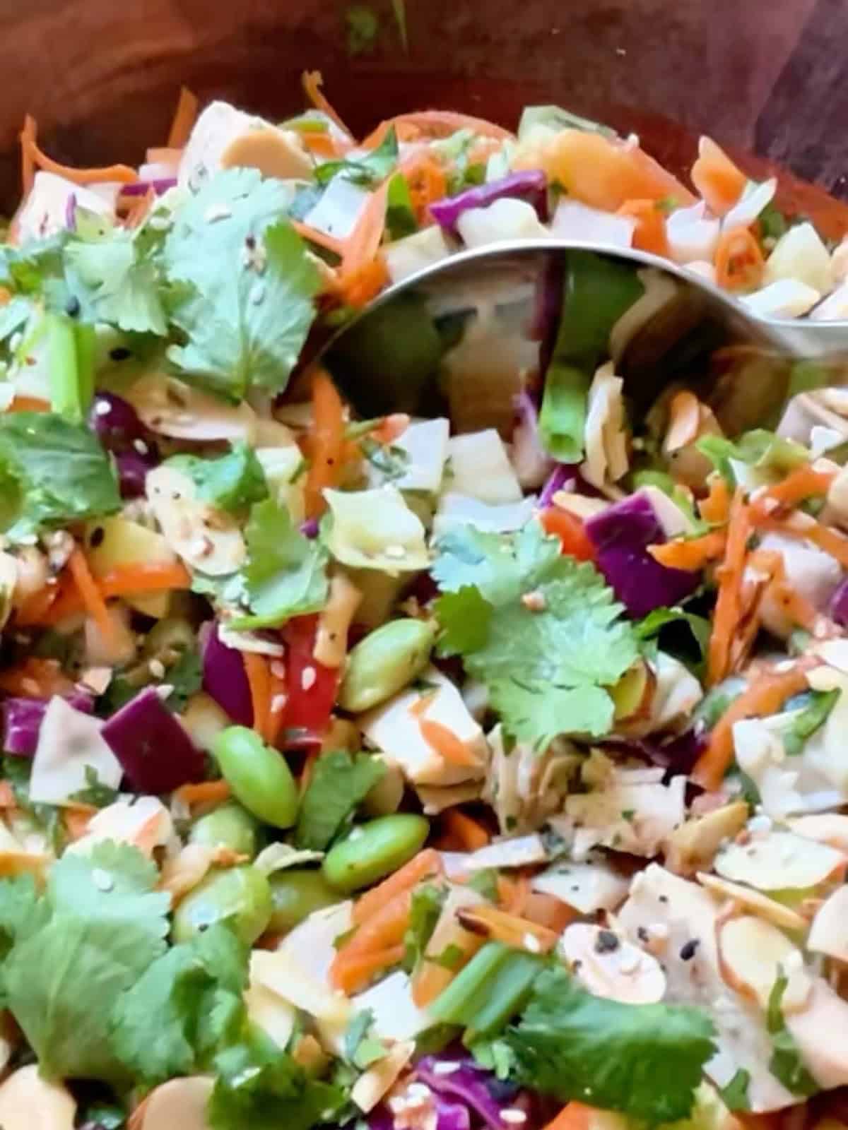 Asian bean salad in a large wooden bowl being dipped with a serving spoon.