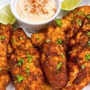 Chicken tenders in white platter with chipotle lime sauce, lime wedges, and cilantro garnish.