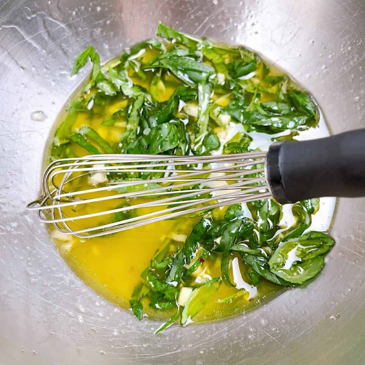 Dressing with basil whisked in a stainless bowl.