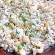 Tuna pasta and peas with dill garnish in a wooden salad bowl.