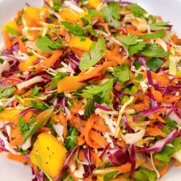 Mango coleslaw in a white bowl with cilantro garnish.