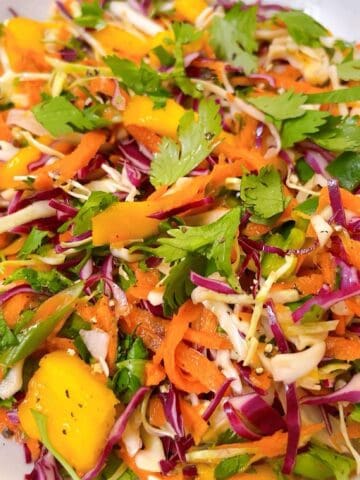 Mango coleslaw in a white bowl with cilantro garnish.