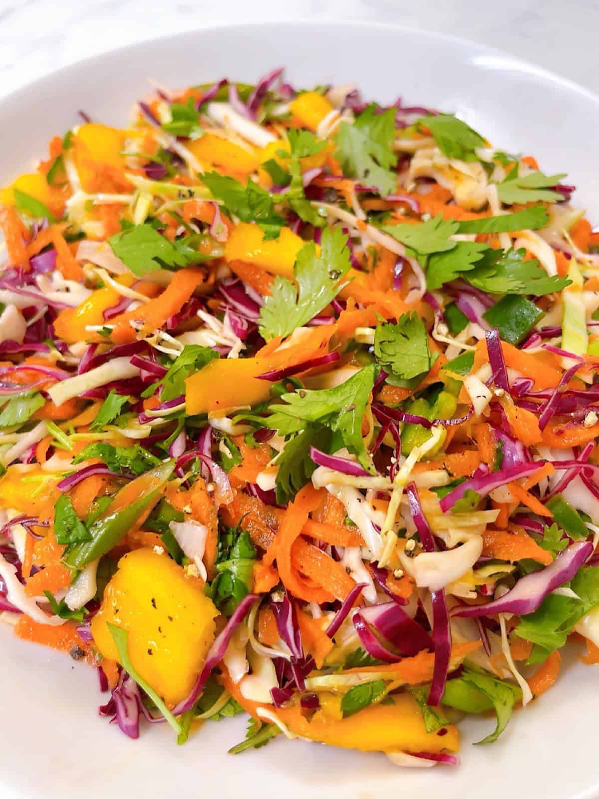 Mango coleslaw in a white bowl with cilantro garnish.